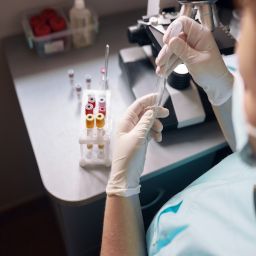 Female lab tech in latex gloves takes sample from test tube with pipette to research material at workplace with modern equipment in office closeup